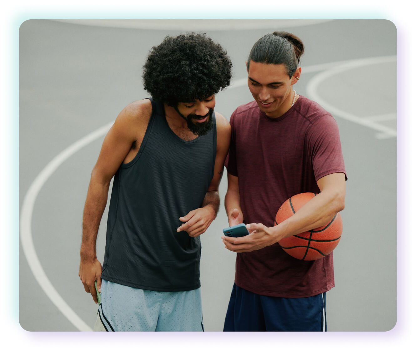 2 friends looking at phone on a basketball court